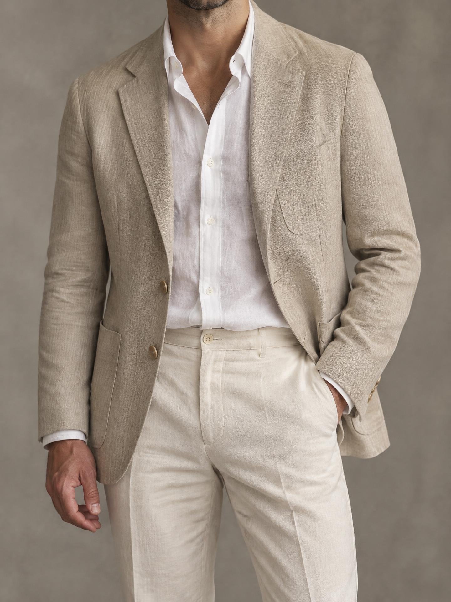 Man in an unstructured sand linen jacket over a white linen shirt and cream linen trousers