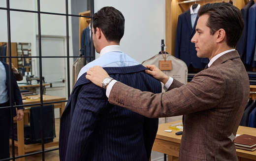 Tailor adjusting a navy pinstripe suit jacket on a client in front of a gridded mirror
